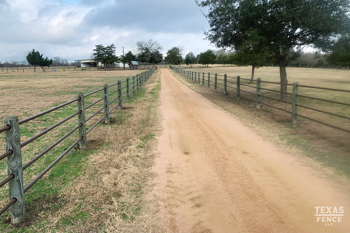 Custom metal pipe and wooden post driveway fencing installed on a farm property by Texas Fence.
